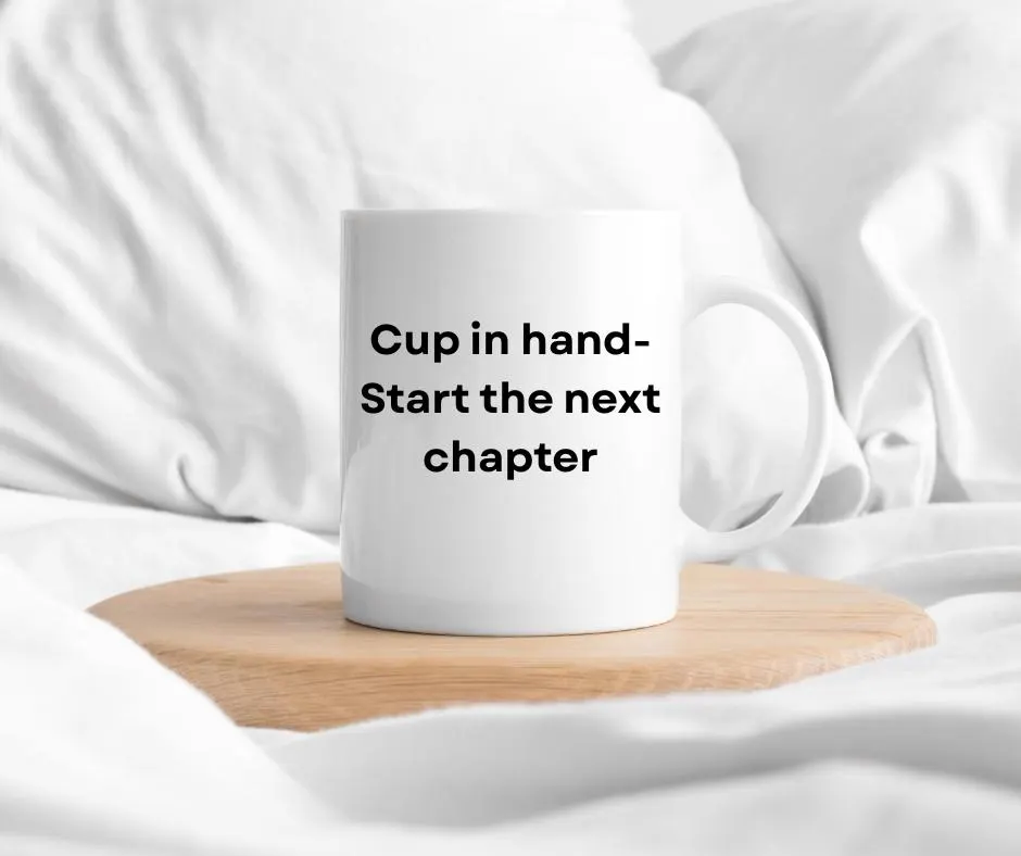 White mug with text 'Cup in hand- Start the next chapter' on a wooden coaster in bed with white fabric background