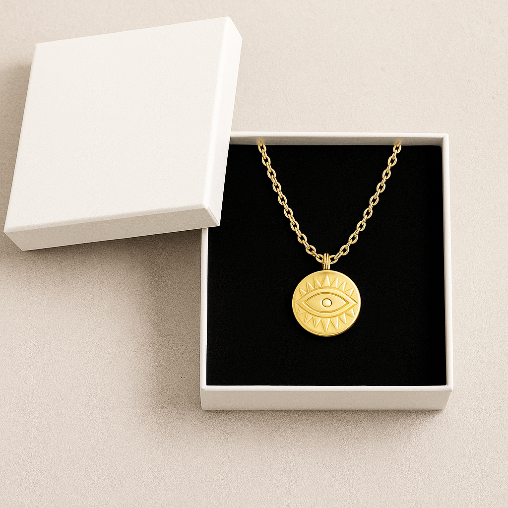 Gold necklace with an evil eye pendant in an open white jewelry box on a beige surface