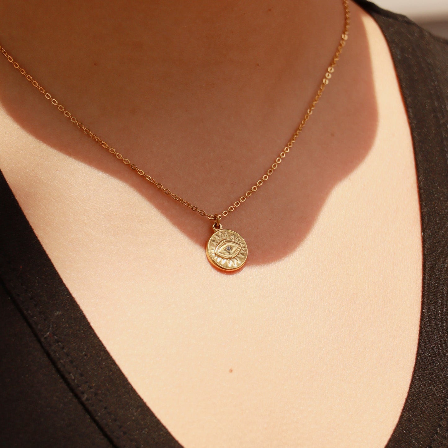Gold necklace with an evil eye pendant on a person wearing a black top.