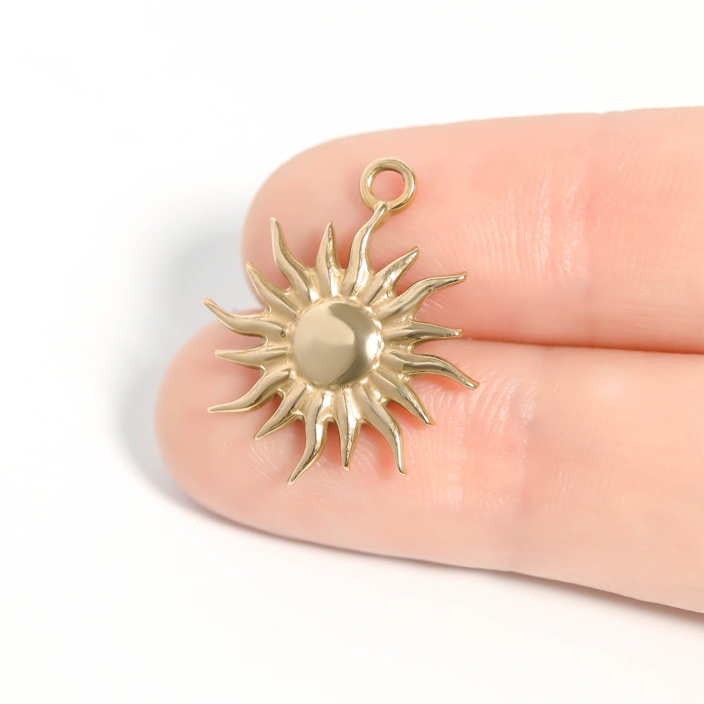Gold sun-shaped pendant held between fingers on a white background