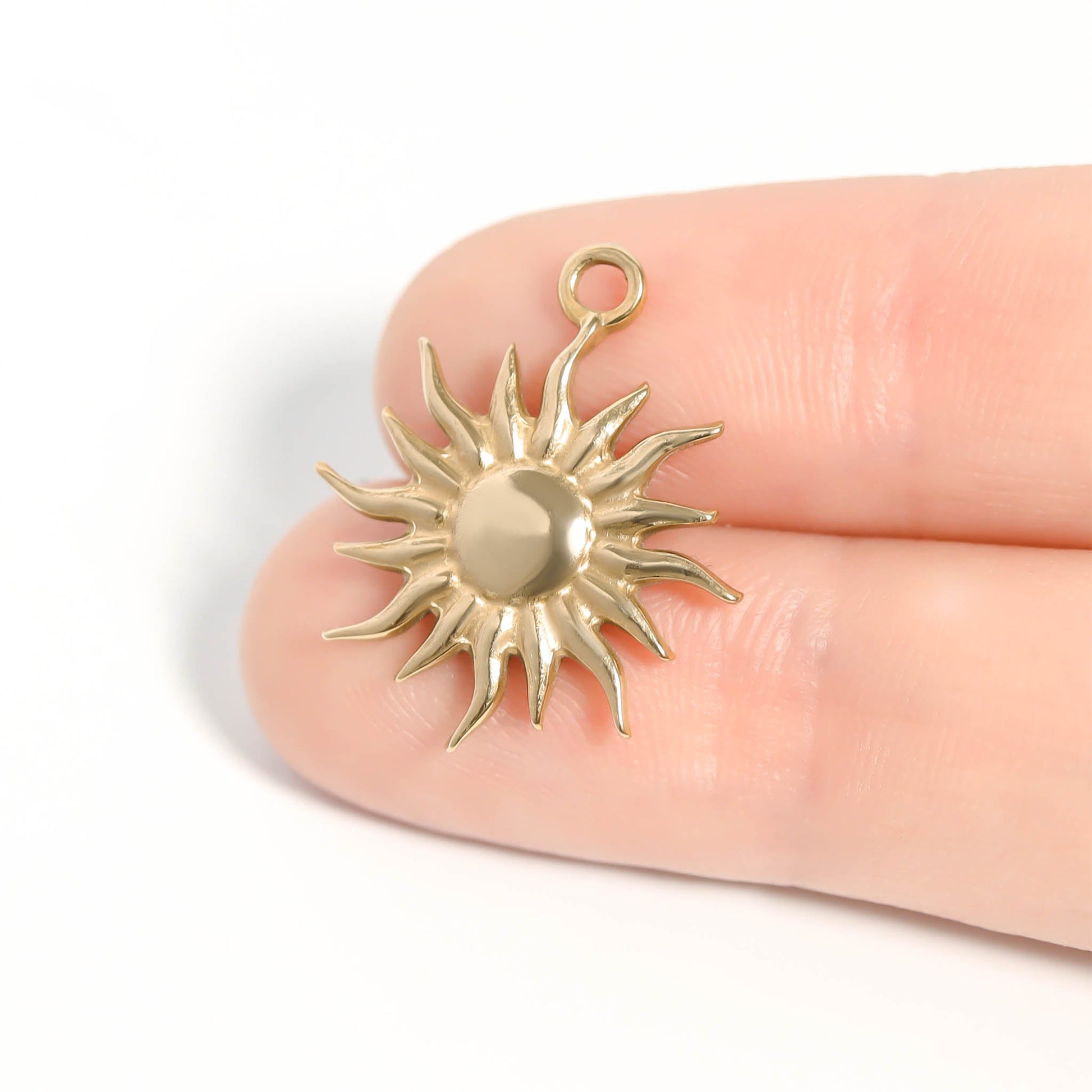 Gold sun-shaped pendant held between fingers on a white background