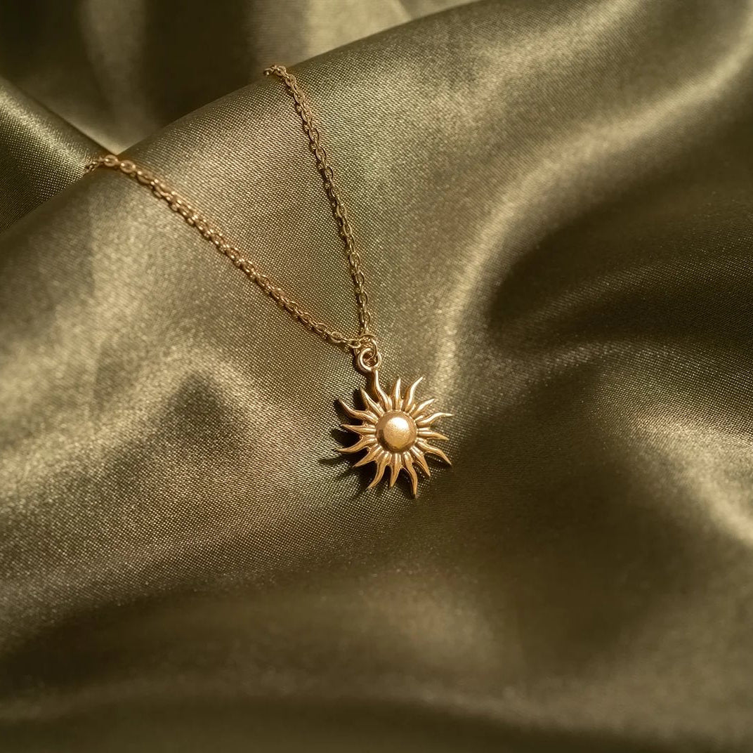 Gold sun-shaped pendant necklace on a gold satin background