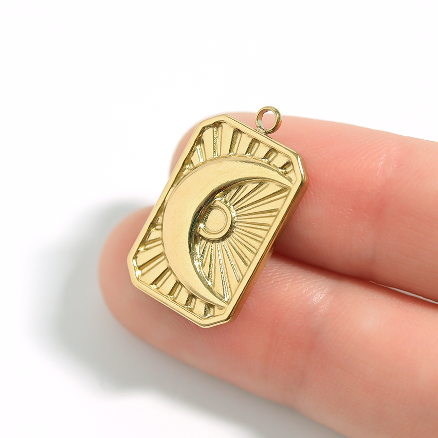 Gold Sunburst Moon pendant held between fingers on a white background