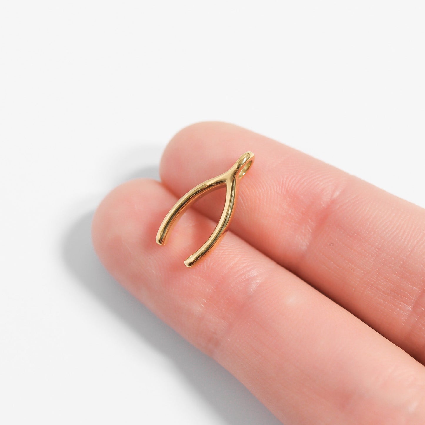 Gold wishbone pendant on a finger against a white background