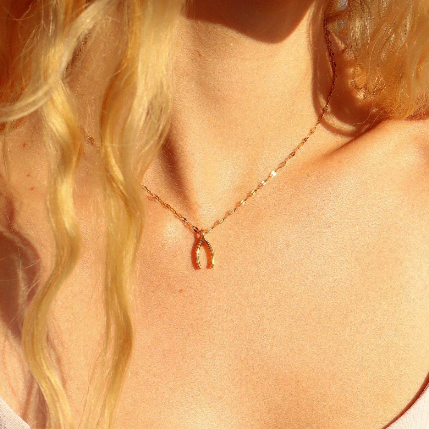 Close-up of a person wearing a gold necklace with a wishbone pendant.