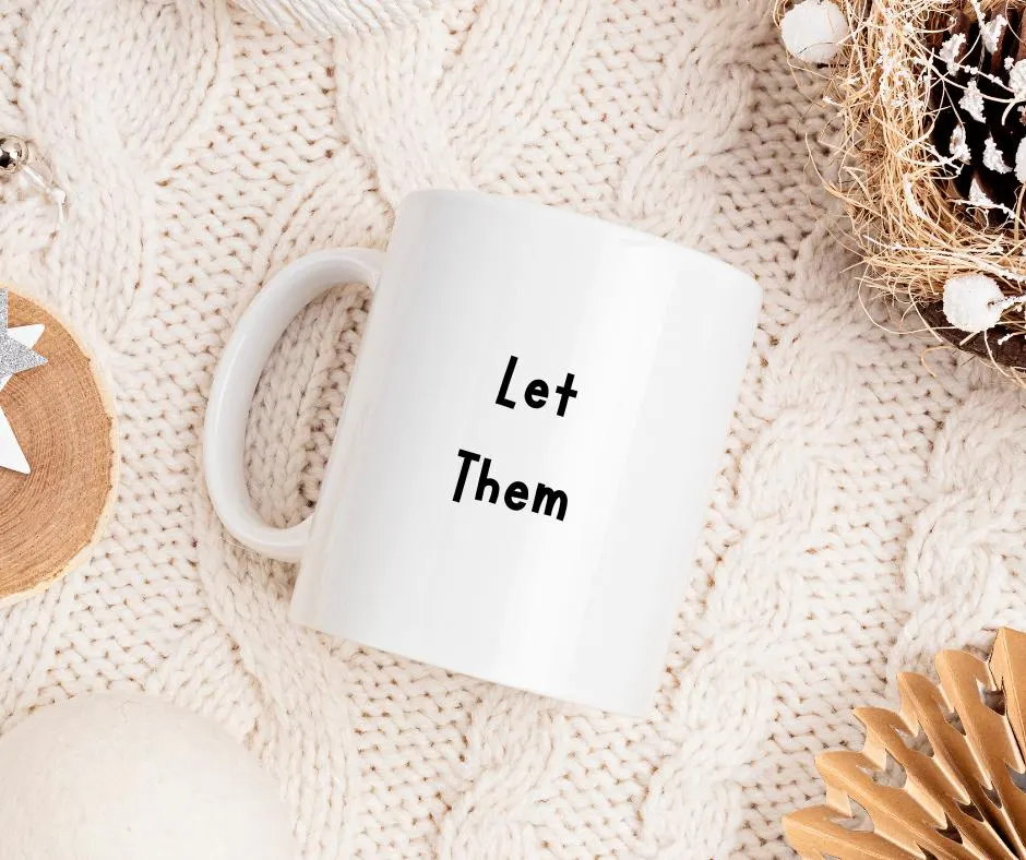 White mug with 'Let Them' text on a textured beige surface