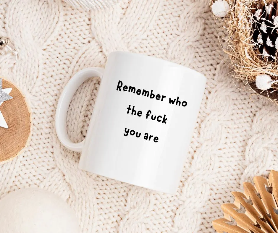 White mug with text 'Remember who the fuck you are' on a textured surface