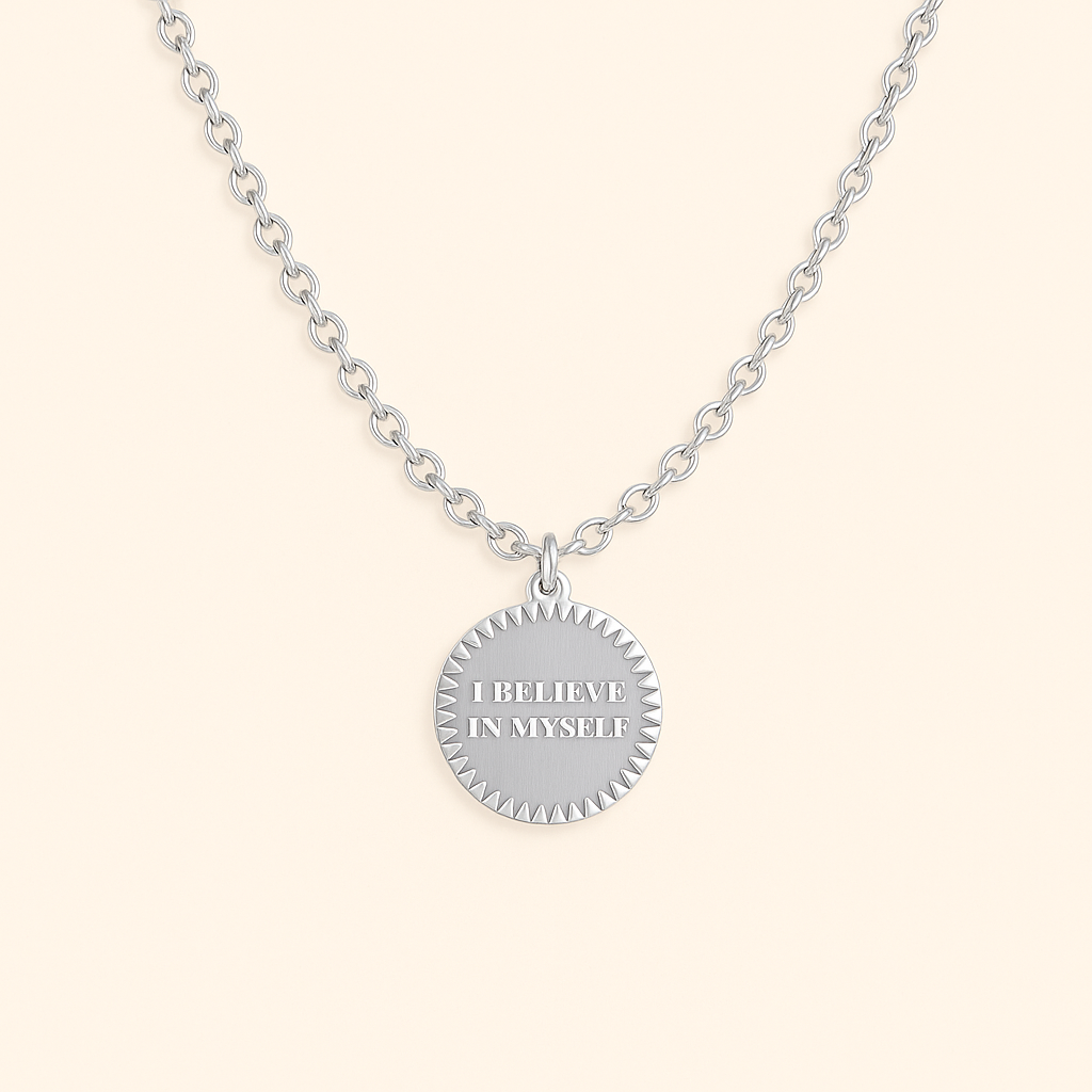 Silver necklace with a round pendant that says 'I believe in myself' on a light beige background