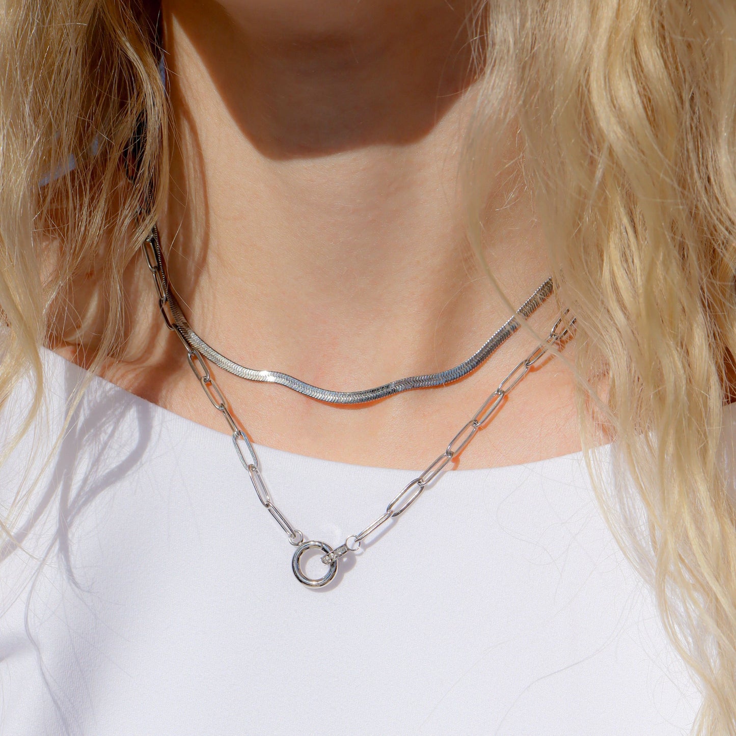 Silver paperclip chain necklace on a person wearing a white top