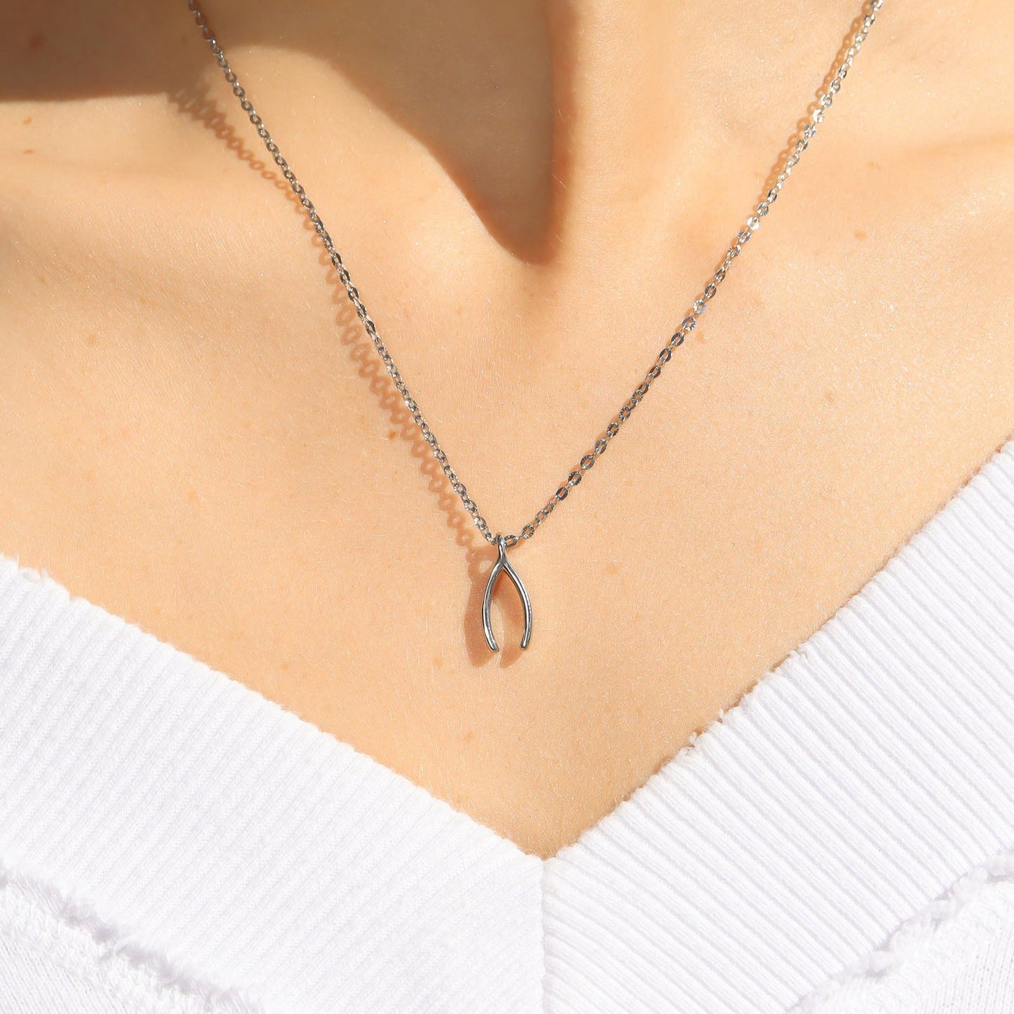 Silver wishbone necklace on a person wearing a white sweater
