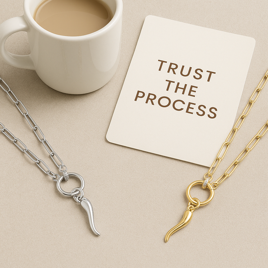 Two necklaces with italian horn pendants on a beige surface next to a cup of coffee and a card with 'Trust the Process' text.