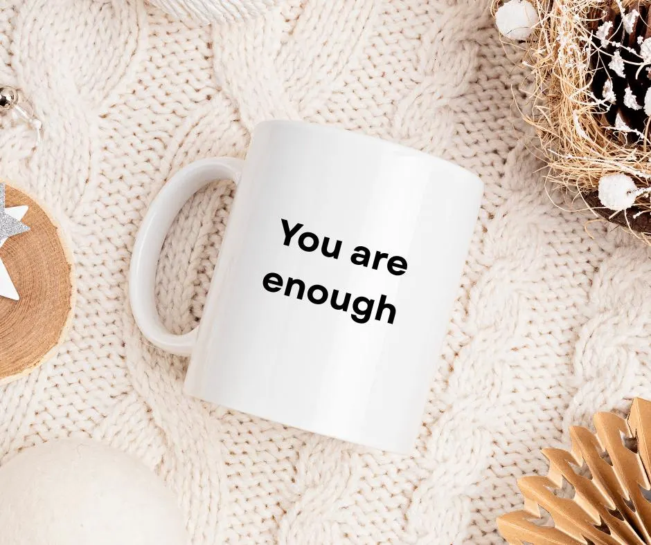White mug with 'You are enough' text on a textured beige surface