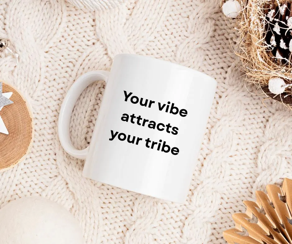 White mug with 'Your vibe attracts your tribe' text on a textured beige surface.